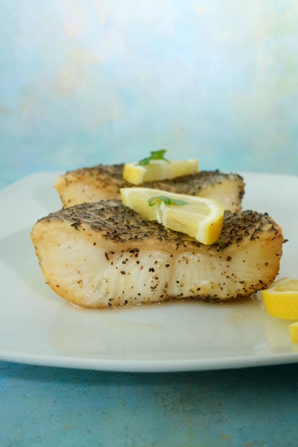 Air fryer Chilean sea bass fillets with crispy skin topped with lemon wedges on a white plate.