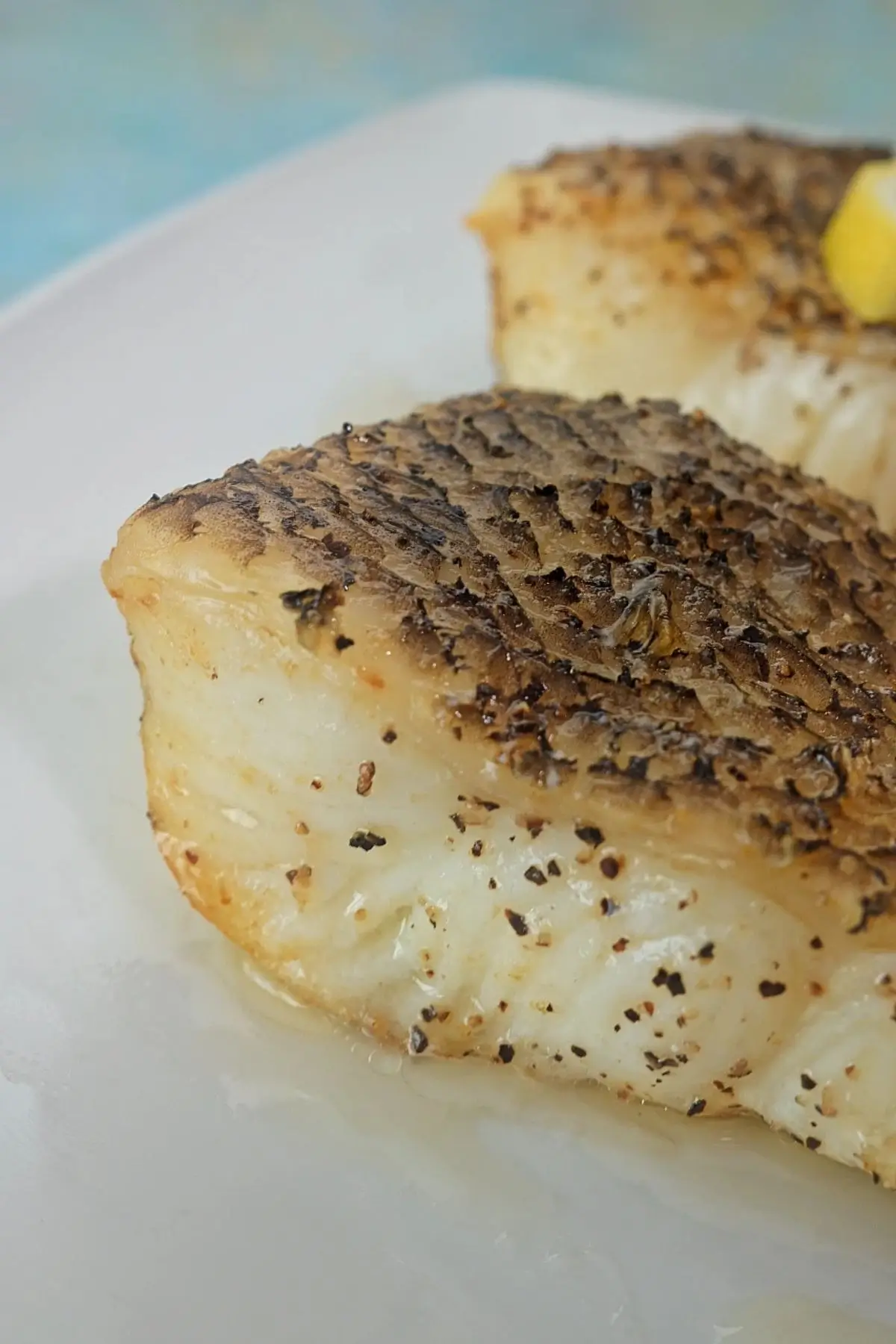 Close-up of crispy skin air fryer Chilean sea bass with lemon wedge garnish on white plate.