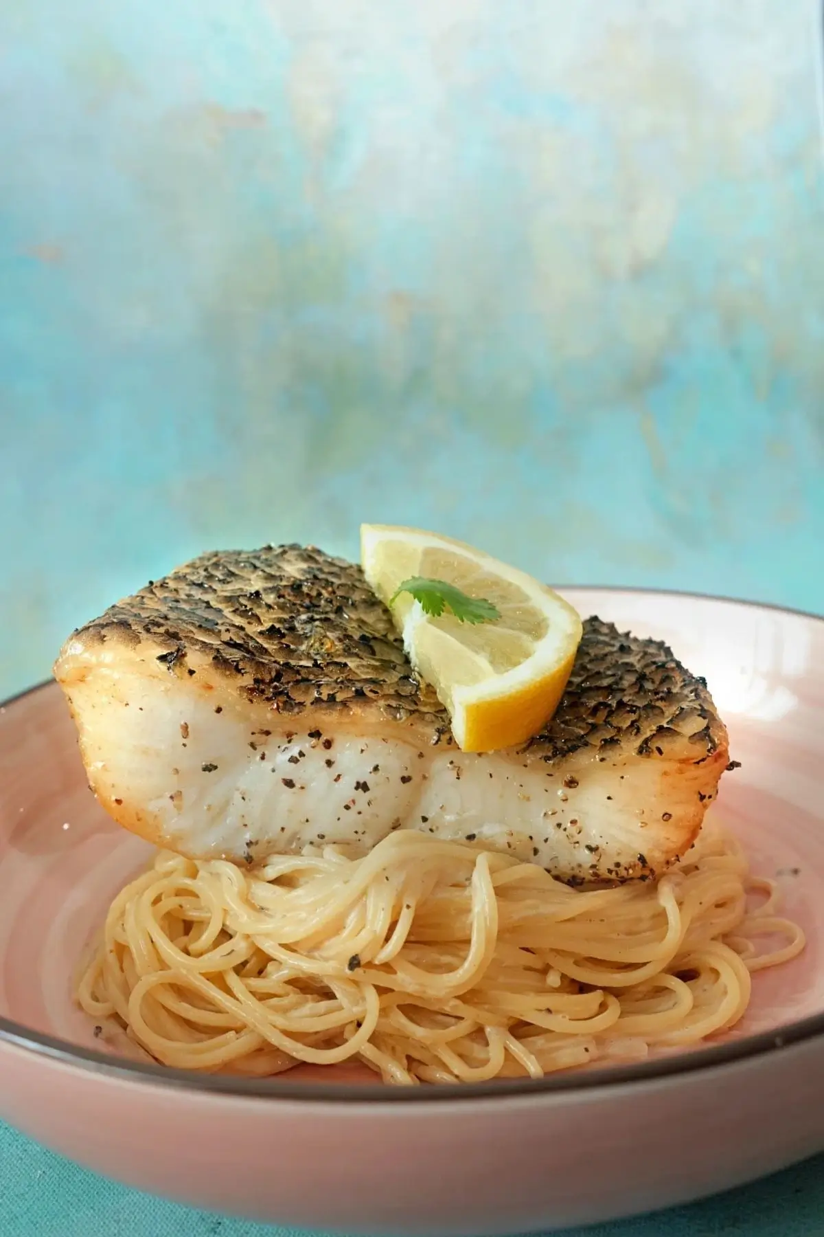 Juicy air fryer Chilean sea bass with cracked pepper and lemon garnish over pasta.