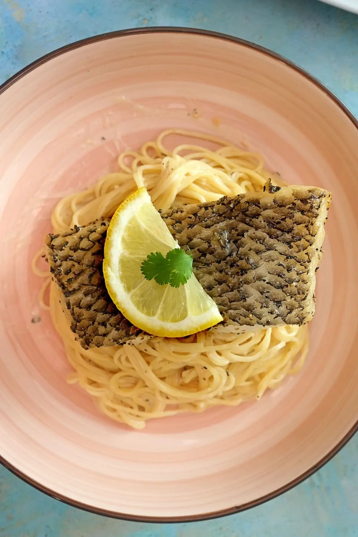 Overhead shot of air fryer Chilean sea bass on buttered spaghetti with lemon slice.