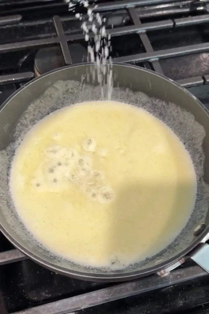 Salt being sprinkled into bubbling melted butter in a pan on the stove.
