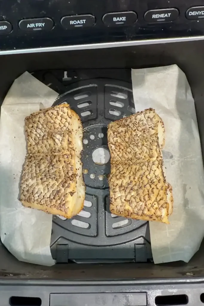 Cooked sea bass fillets in an air fryer basket with lightly crisped skin and golden edges.