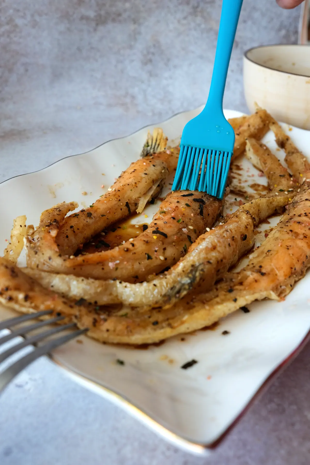 Silicone brush glazing crispy salmon belly pieces on a white plate.