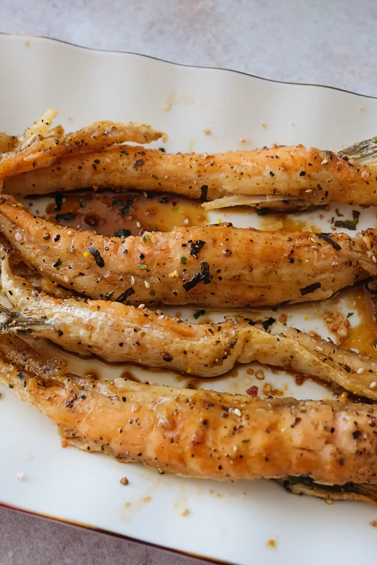 Crispy salmon belly pieces drizzled with sauce on a serving platter.