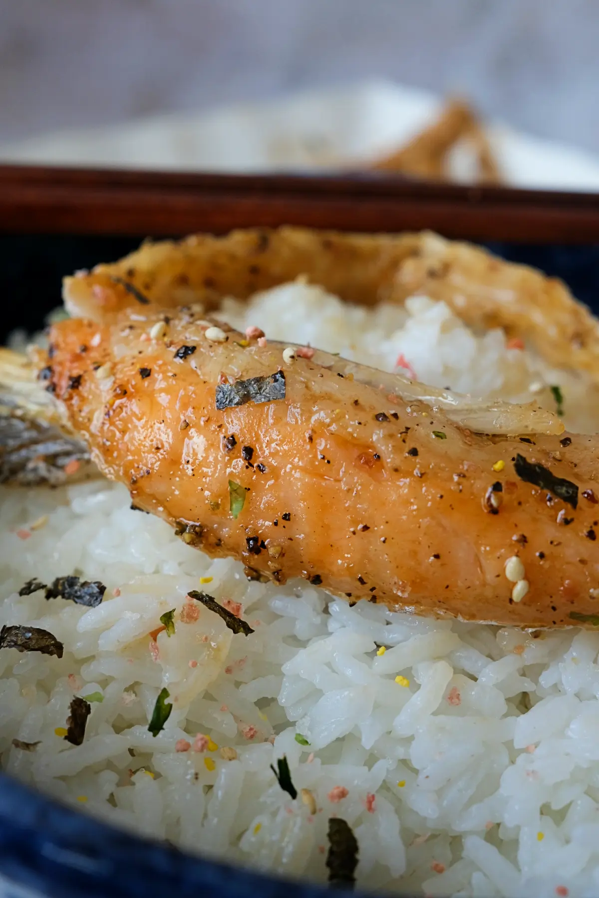 Glazed salmon belly resting on a bowl of steamed white rice with furikake.