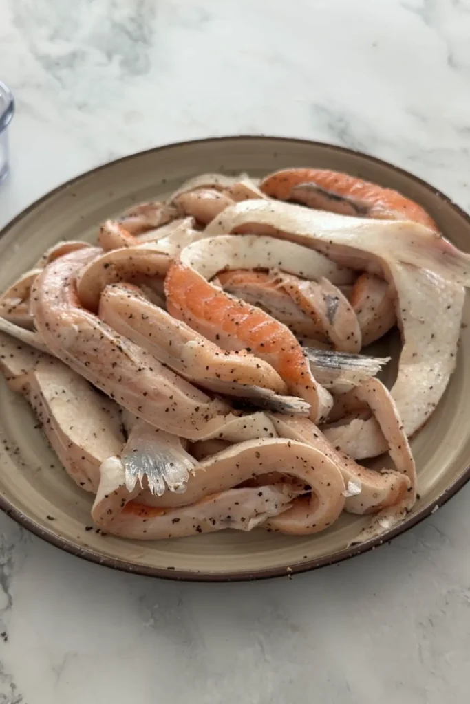 Raw salmon belly seasoned with salt and pepper on a plate.
