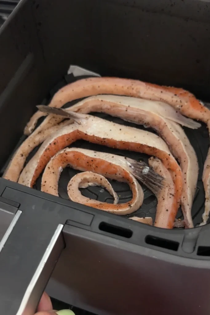 Cookd salmon belly in an air fryer basket.