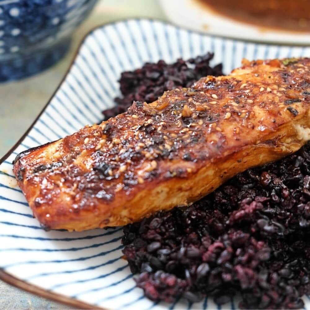 Air fryer teriyaki salmon fillet glazed with sauce served over black rice.