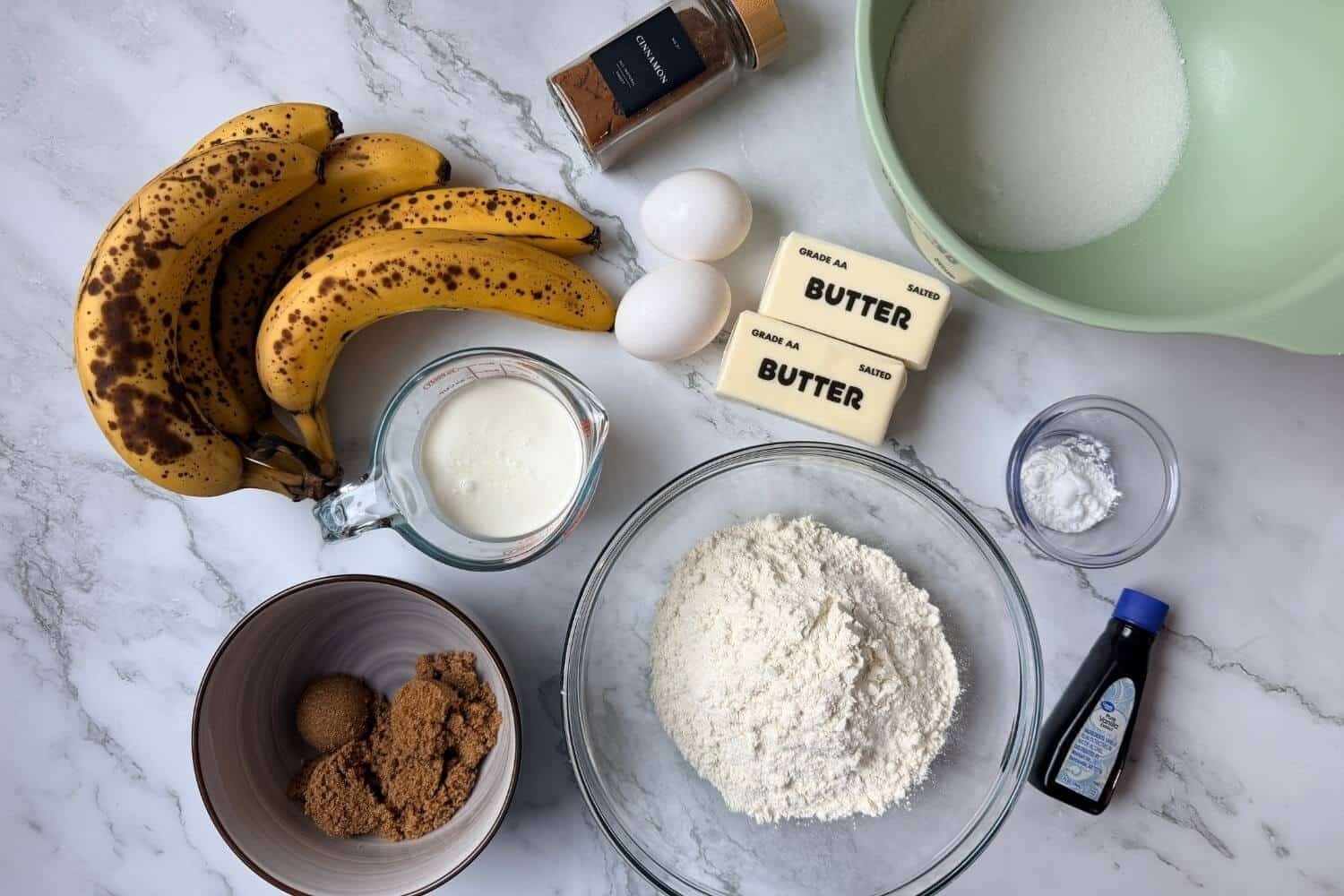 Ingredients for banana bread: ripe bananas, butter, eggs, sugar, flour, baking powder, baking soda, vanilla, cream, brown sugar, and cinnamon.