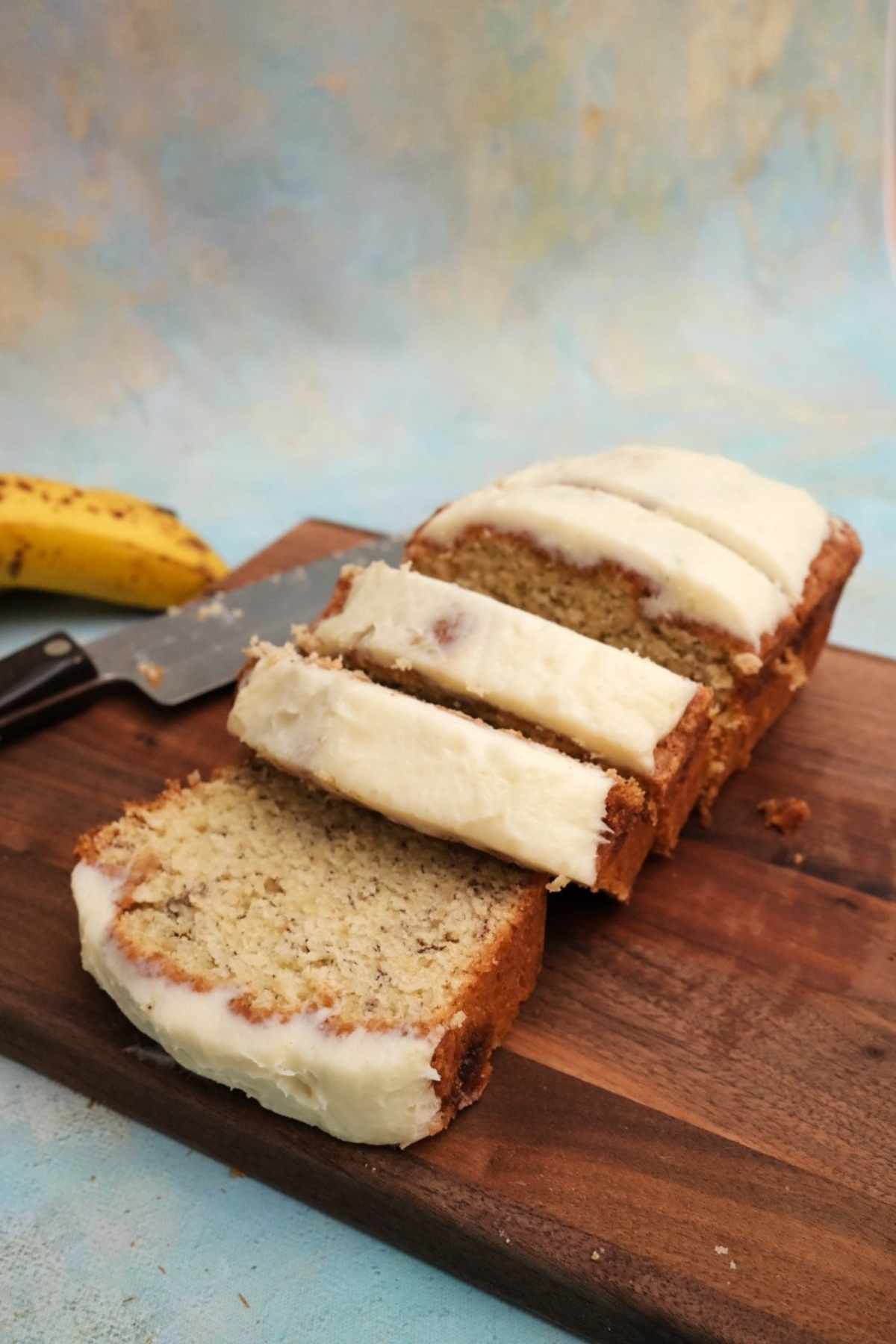 Close-up of frosted banana bread slices stacked on a cutting board with soft blue background.