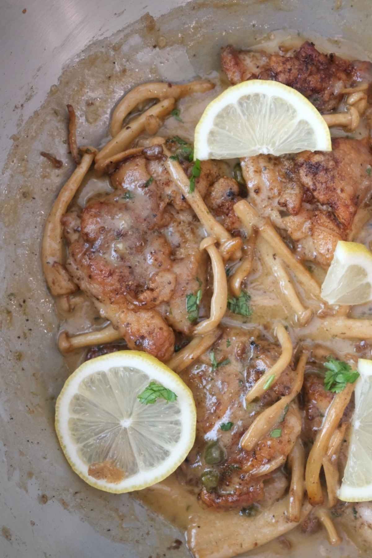Creamy chicken piccata with mushrooms, capers, and lemon slices in a skillet
