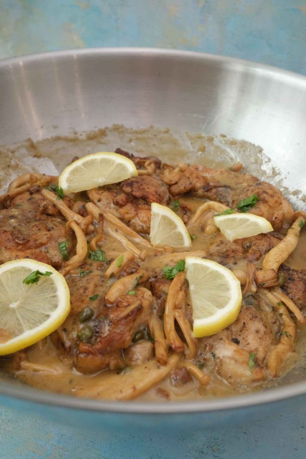 Chicken piccata with mushrooms, capers, and lemon slices in a skillet