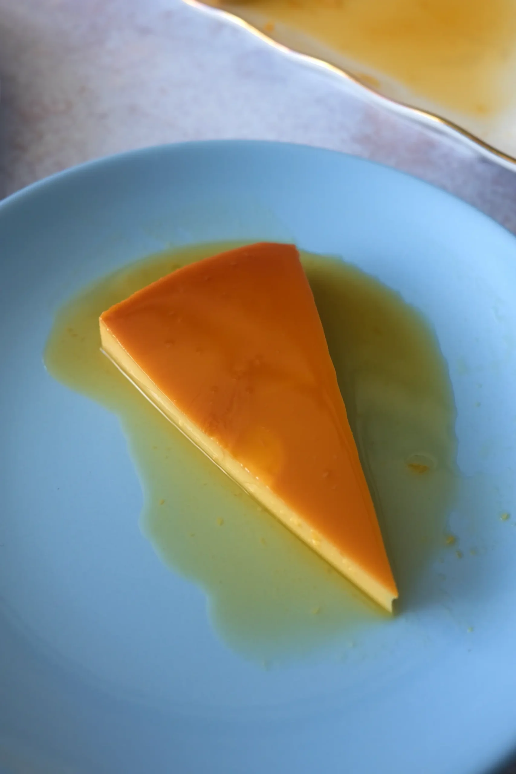 Close-up of creamy leche flan slice with caramel sauce on a blue plate.
