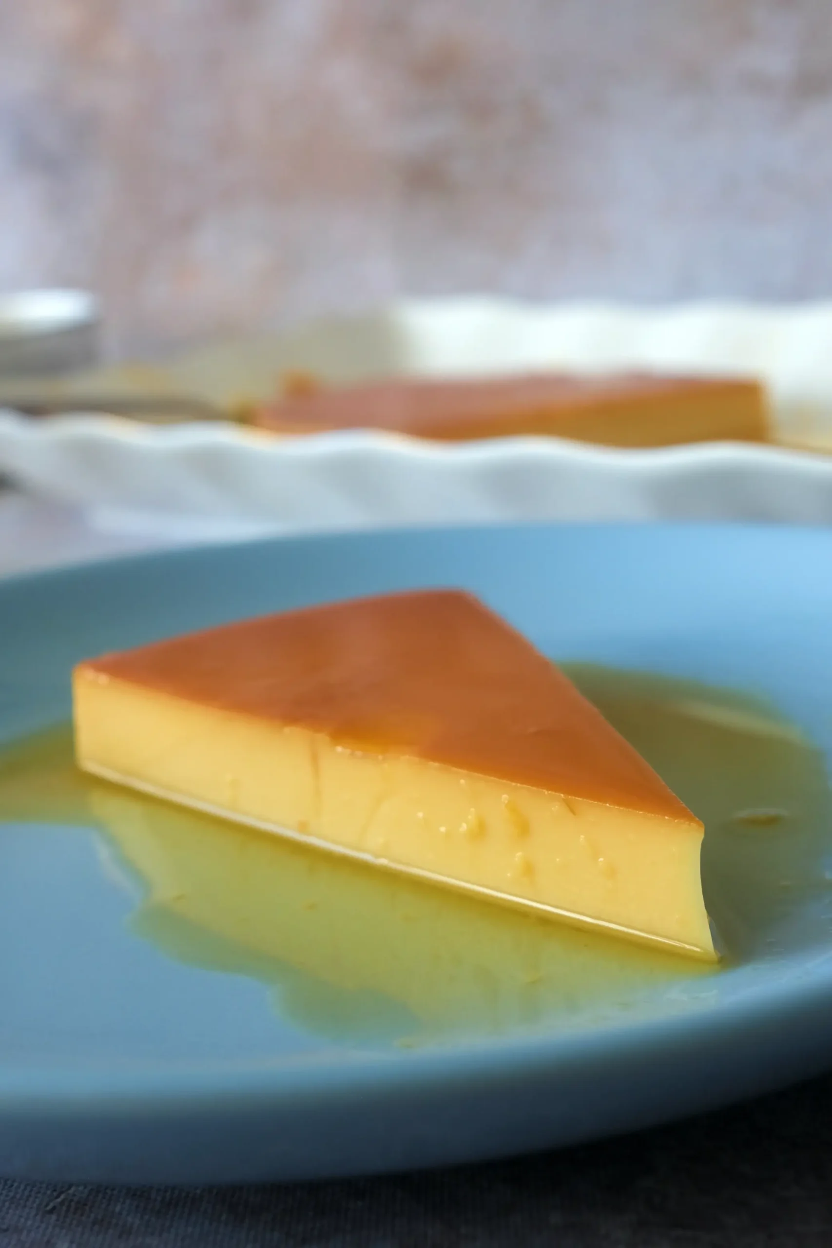 Slice of Filipino leche flan on a blue plate with glossy caramel sauce pooling around it.