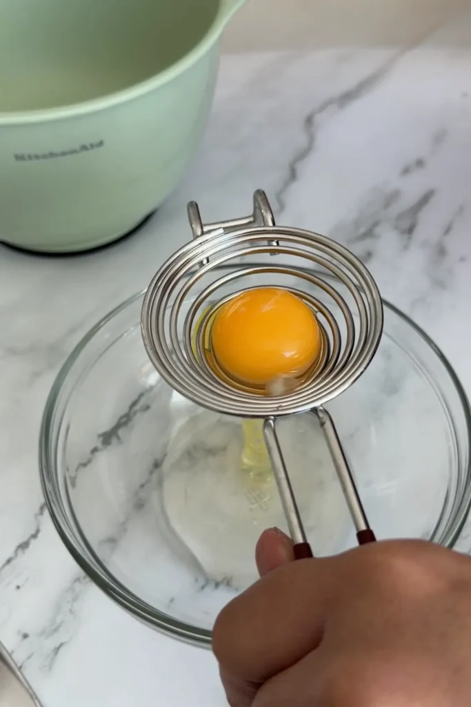 Egg yolk separated from the white using a metal egg separator over a glass bowl.