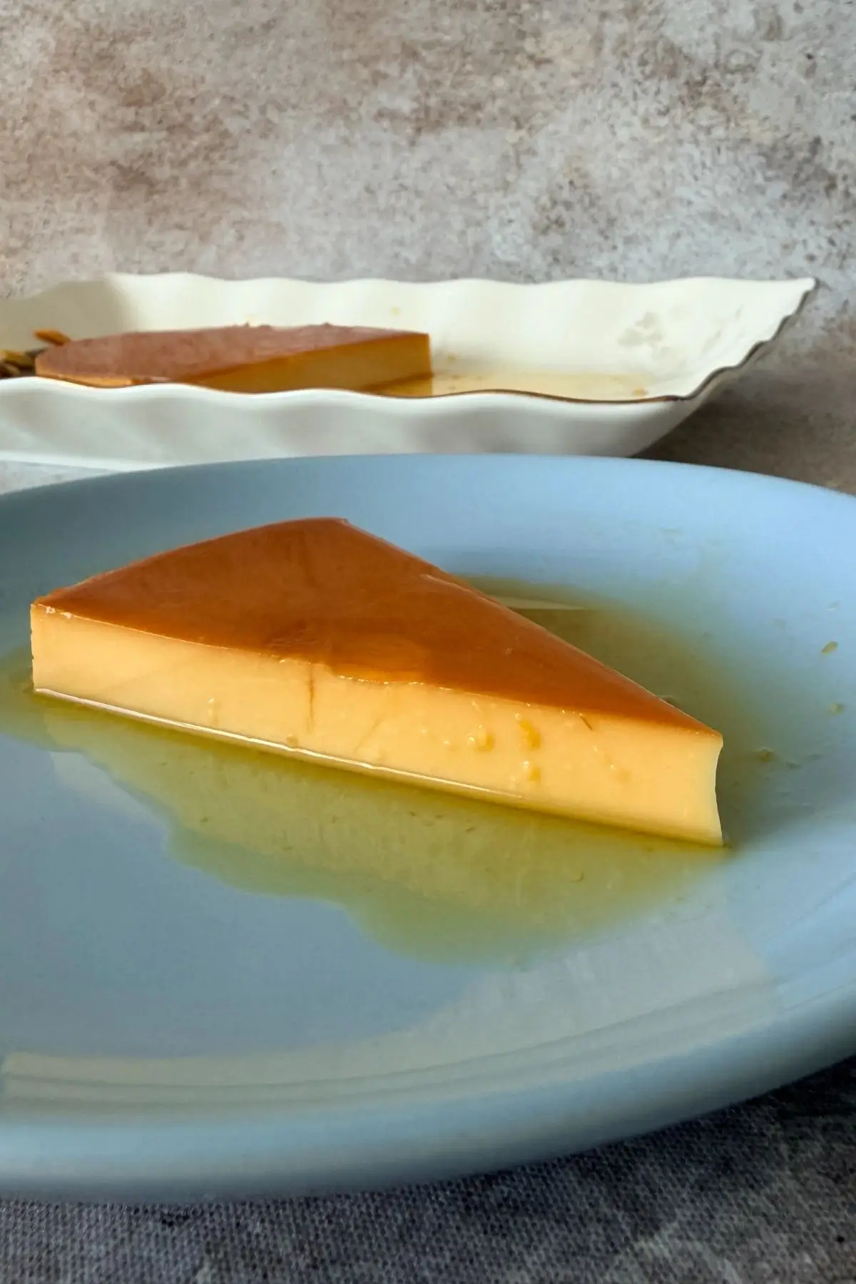 Slice of Filipino leche flan on a plate with glossy caramel sauce pooling around it.