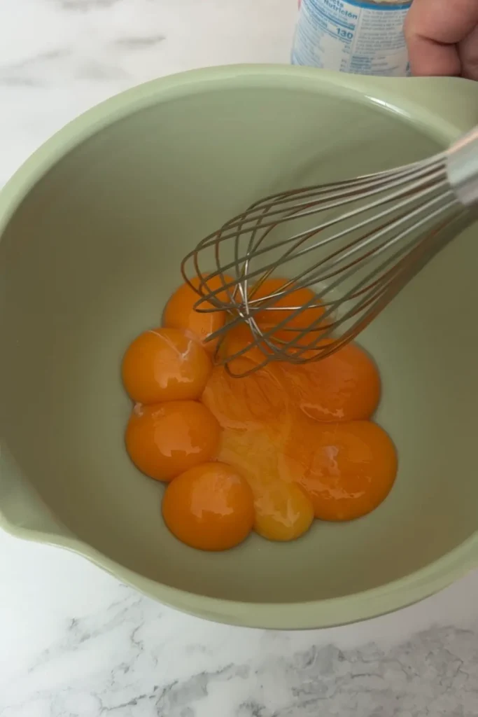 Whisk gently mixing egg yolks in a light green bowl.