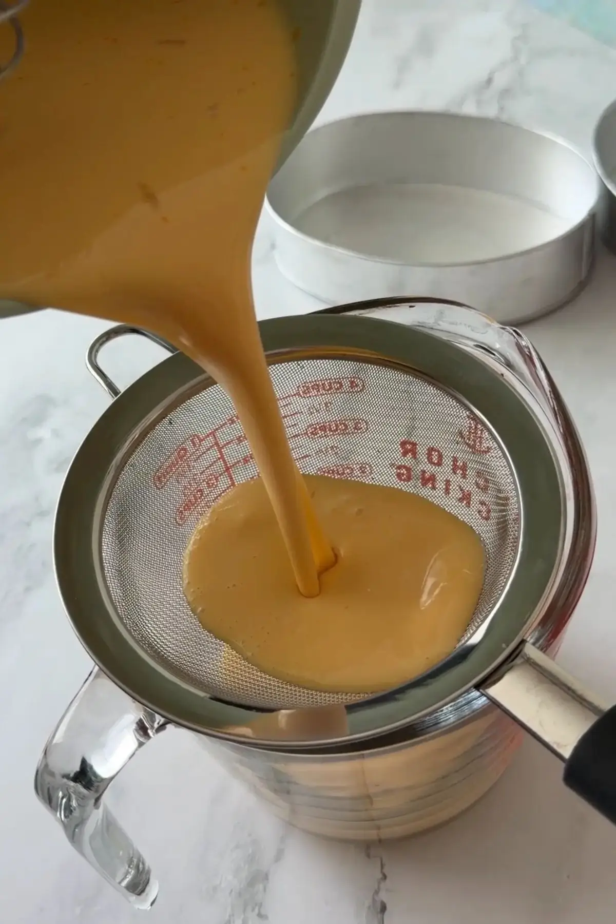 Leche flan mixture strained through a fine mesh sieve into a measuring cup.