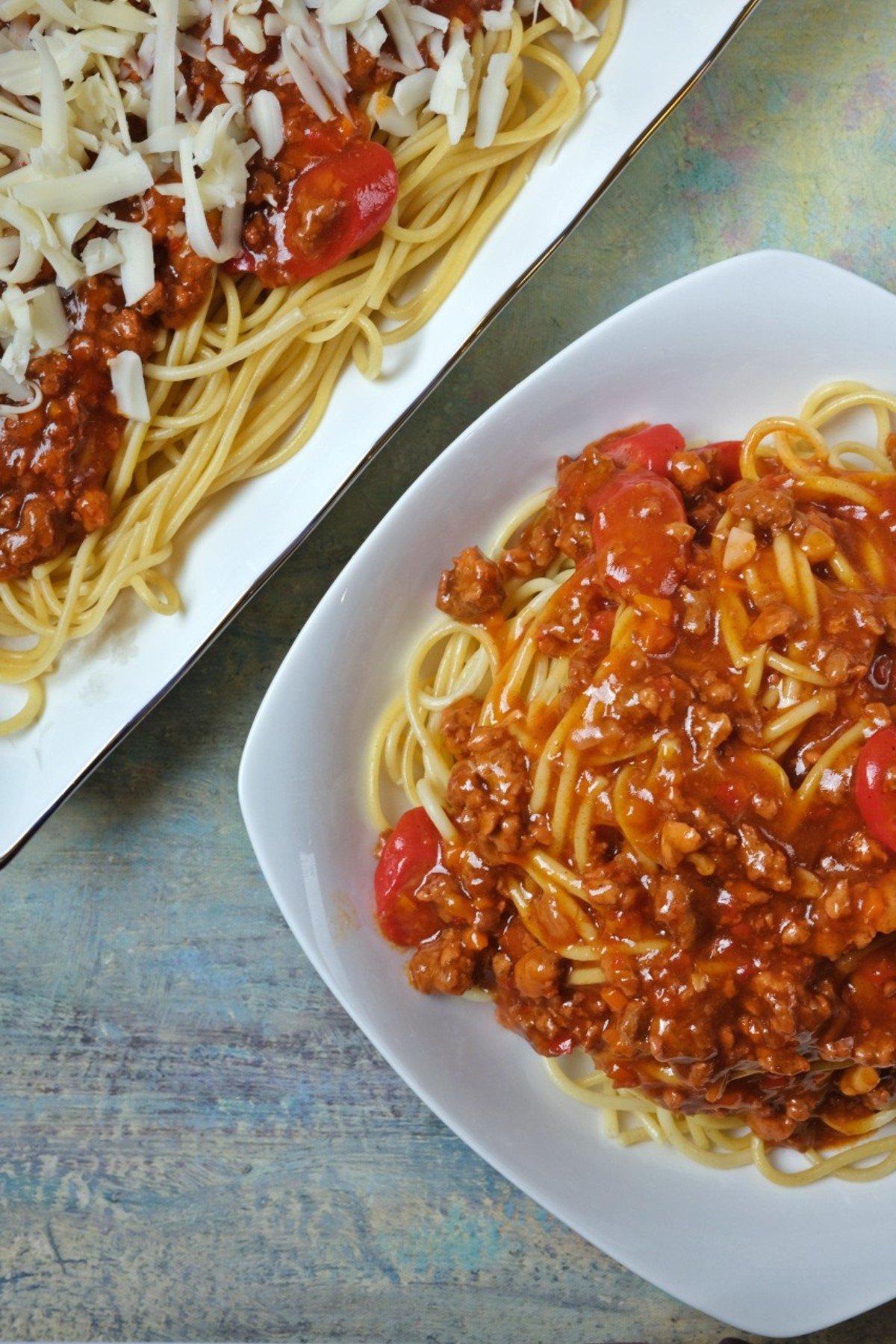 Filipino spaghetti topped with shredded cheese, served in a large dish and on an individual plate.