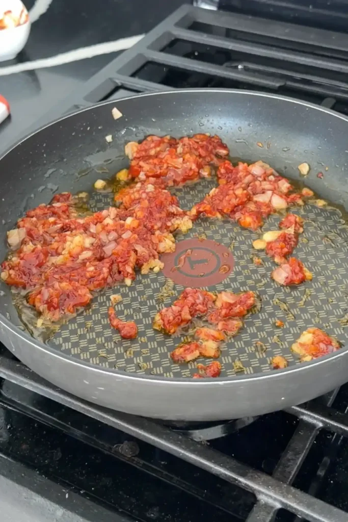 Gochujang added to sautéed garlic and onion, cooking to deepen color and flavor.