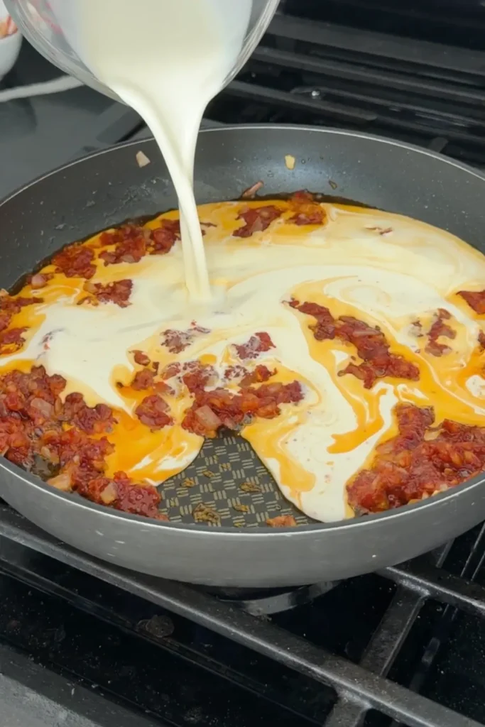 Heavy cream being poured into gochujang mixture to create a creamy pasta sauce.