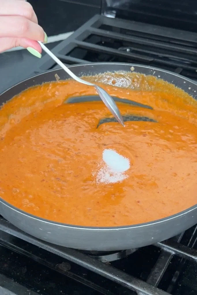 Sugar being added to creamy gochujang sauce while it simmers.