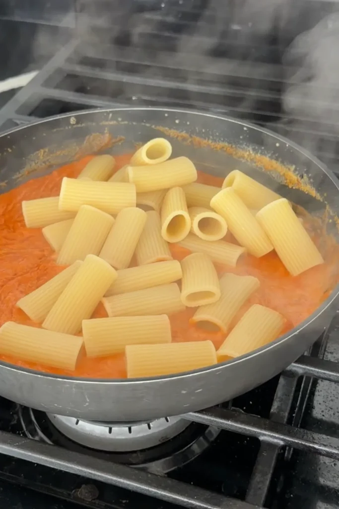 Cooked rigatoni added to the creamy gochujang sauce in a skillet.