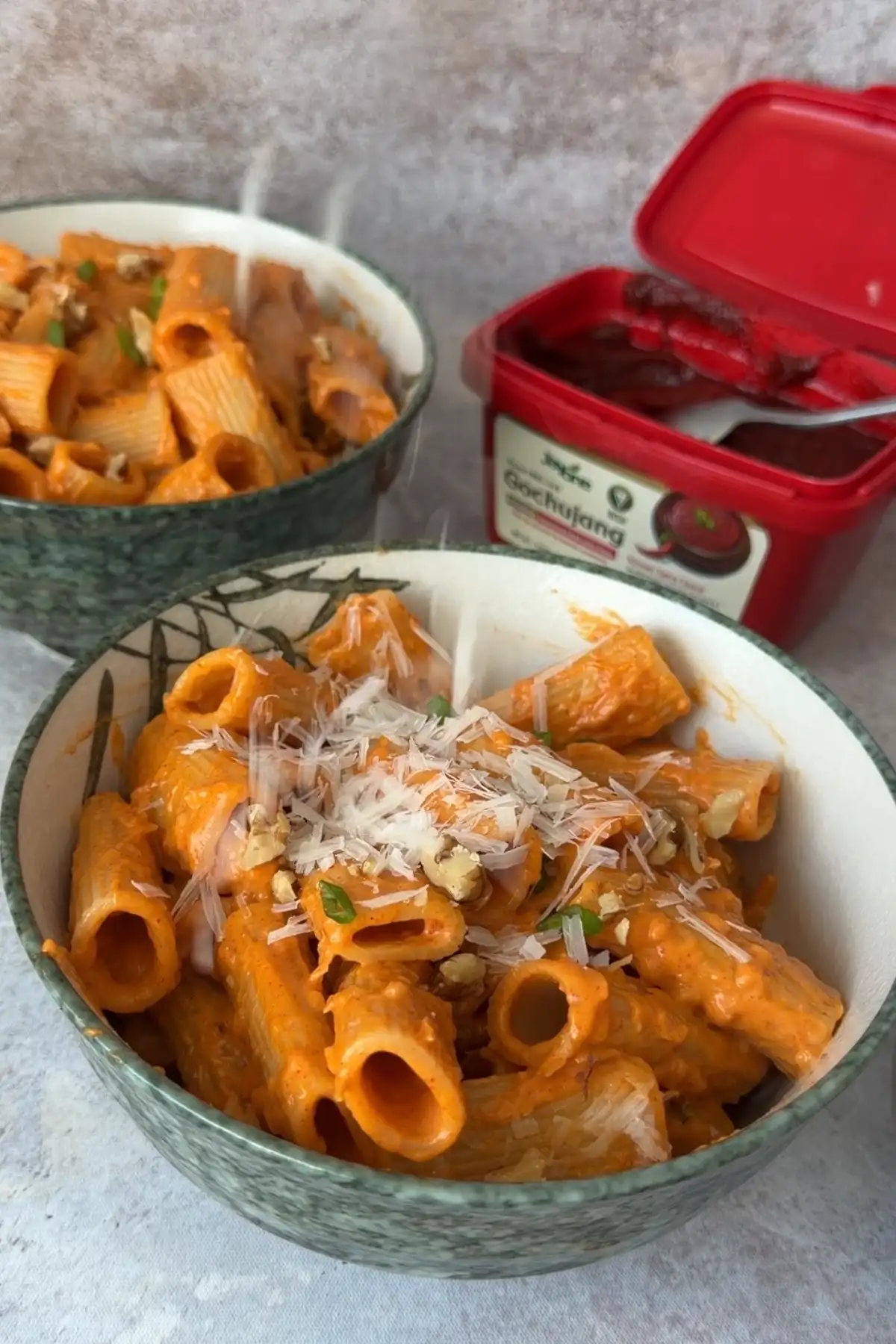 Bowl of creamy gochujang pasta topped with freshly grated Parmesan and chopped walnuts, with gochujang container in the background.