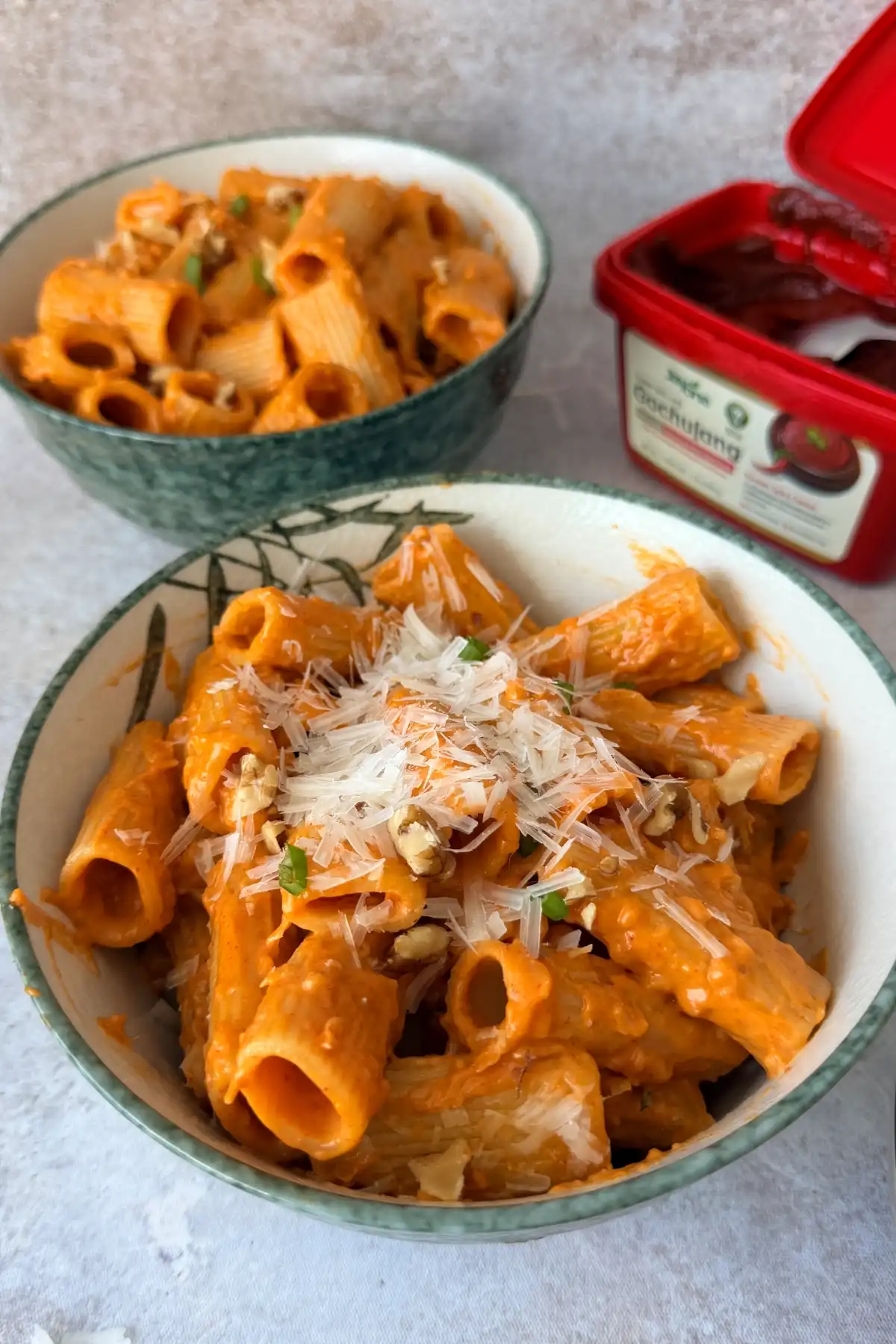 Gochujang pasta served in a bowl with Parmesan and walnuts on top.