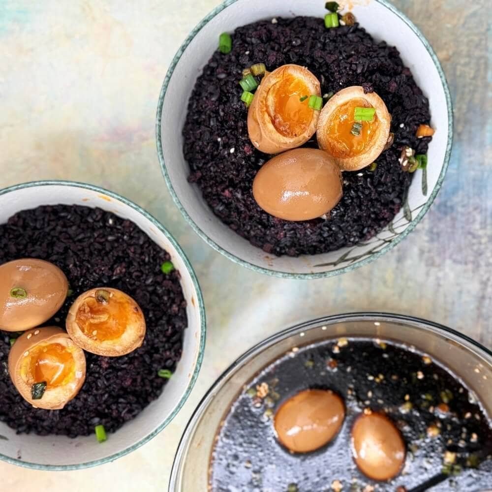 Korean mayak eggs with jammy yolks served over black rice in ceramic bowls