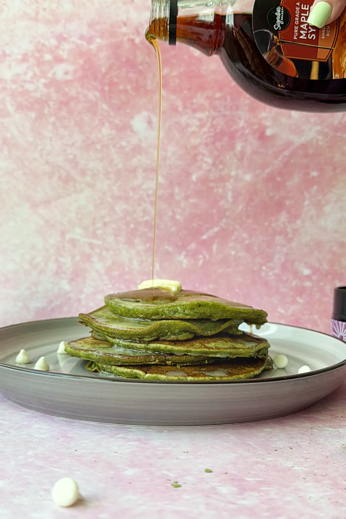 Maple syrup being poured over warm matcha pancakes with butter on top