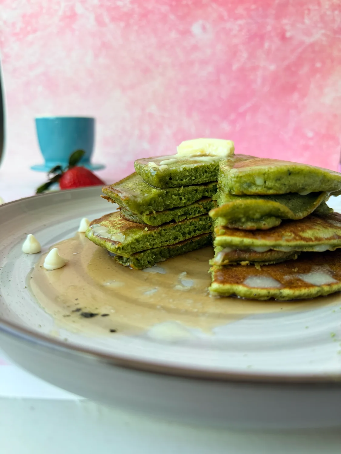 Matcha pancake stack cut into wedges with syrup and strawberries on the side