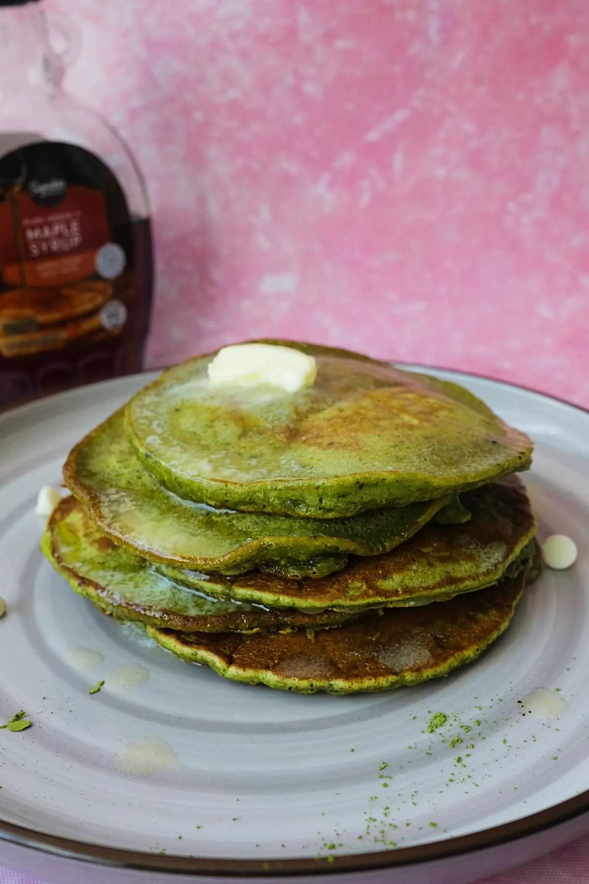 Stack of fluffy matcha pancakes topped with melting butter and maple syrup on a white plate