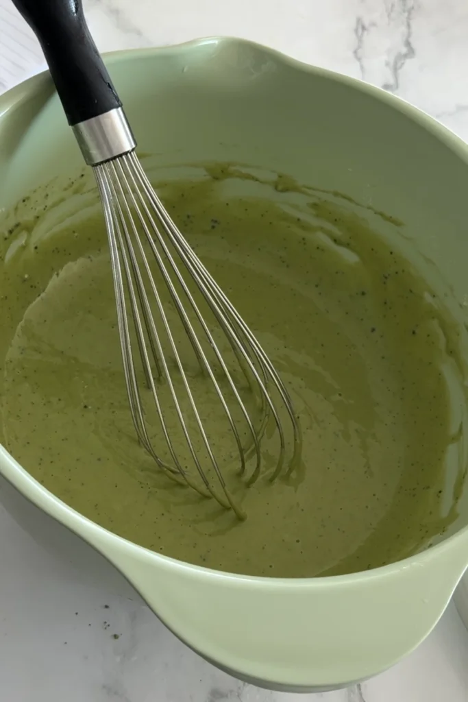 Whisked matcha pancake batter in mixing bowl, smooth and light green with small specks of matcha.