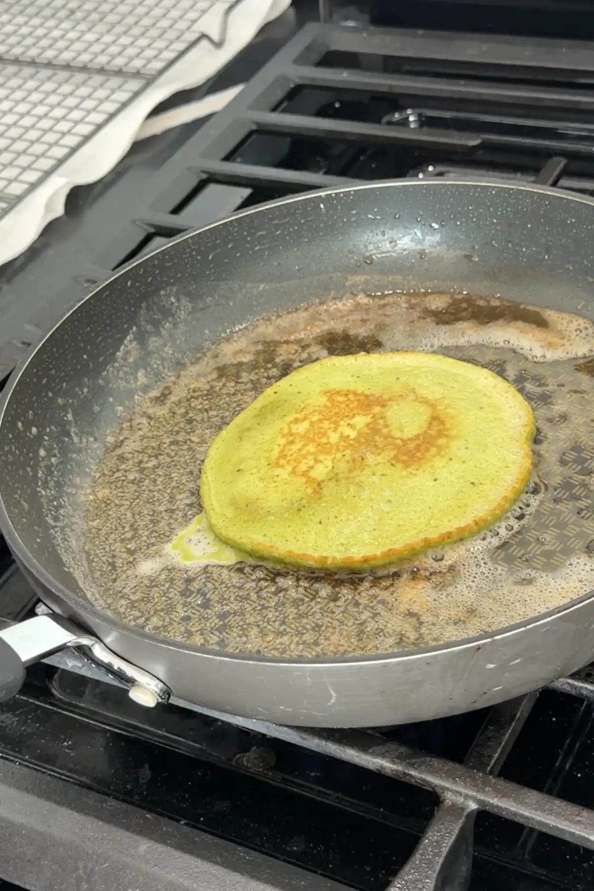 Flipped matcha pancake in skillet showing golden brown center and green edges.