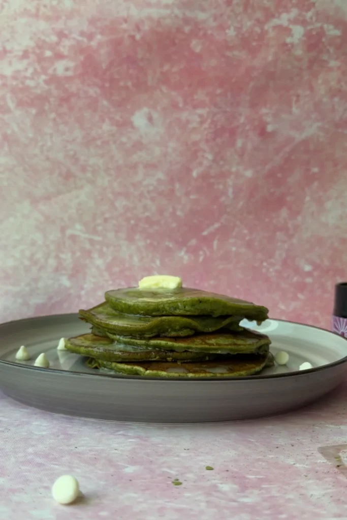 Close-up of matcha pancake stack with melting butter on pink background.