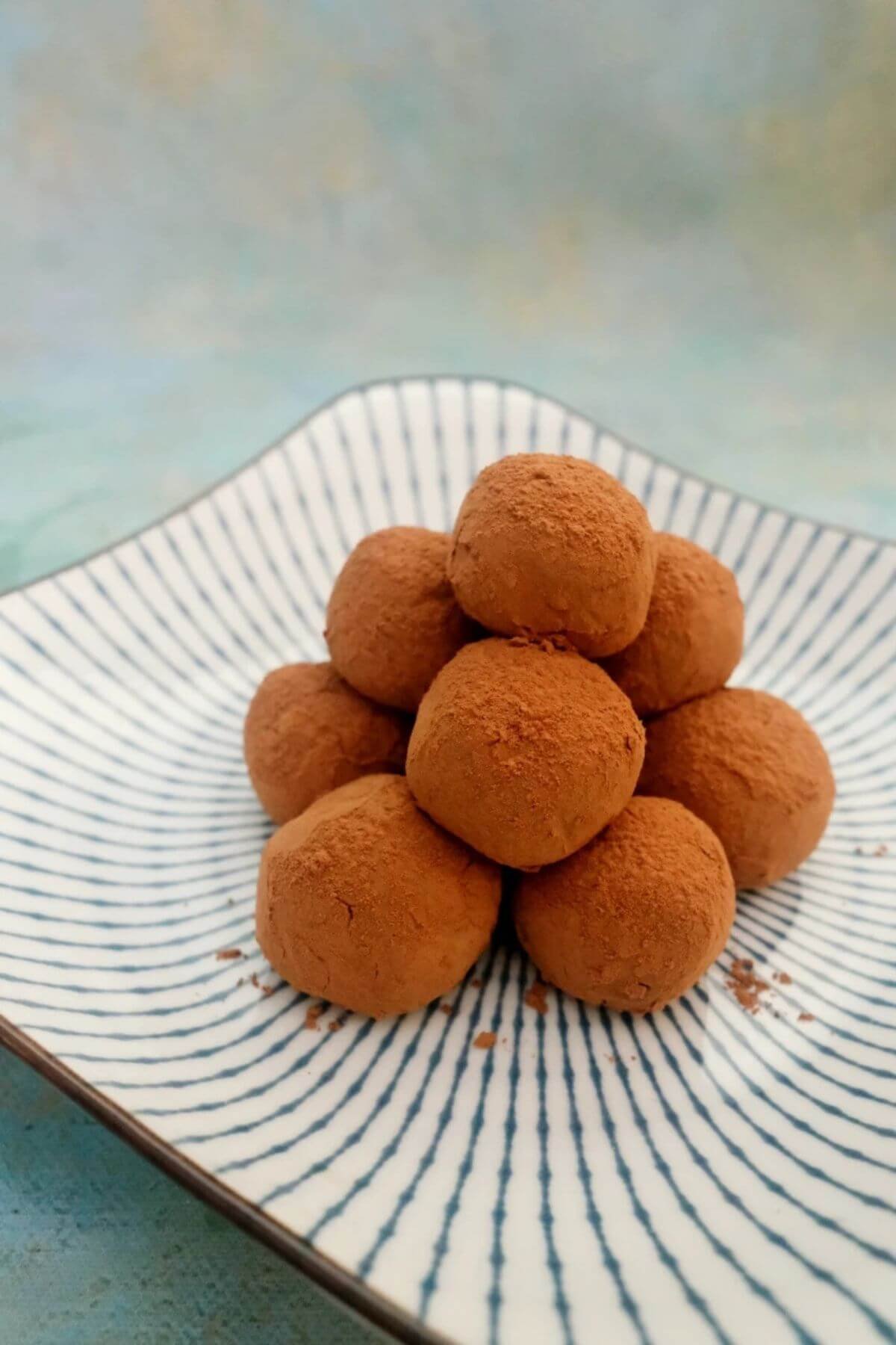 Milk chocolate truffles dusted in cocoa powder stacked on a white striped plate.