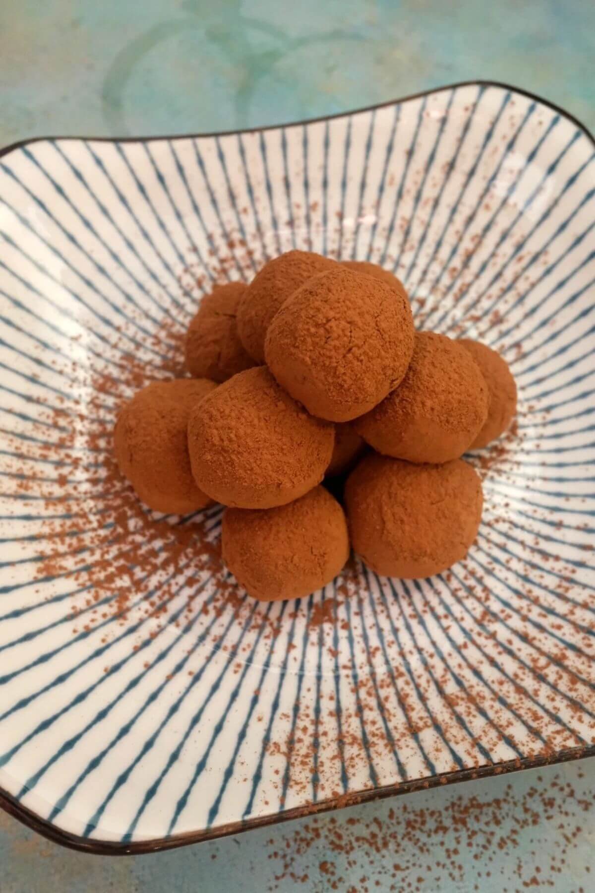 Homemade milk chocolate truffles coated in cocoa powder with extra cocoa dusted around the plate.