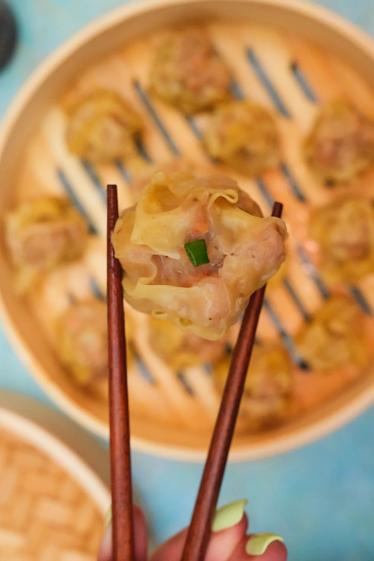 Close-up of pork siomai held with chopsticks showing tender filling and soft wonton wrapper.