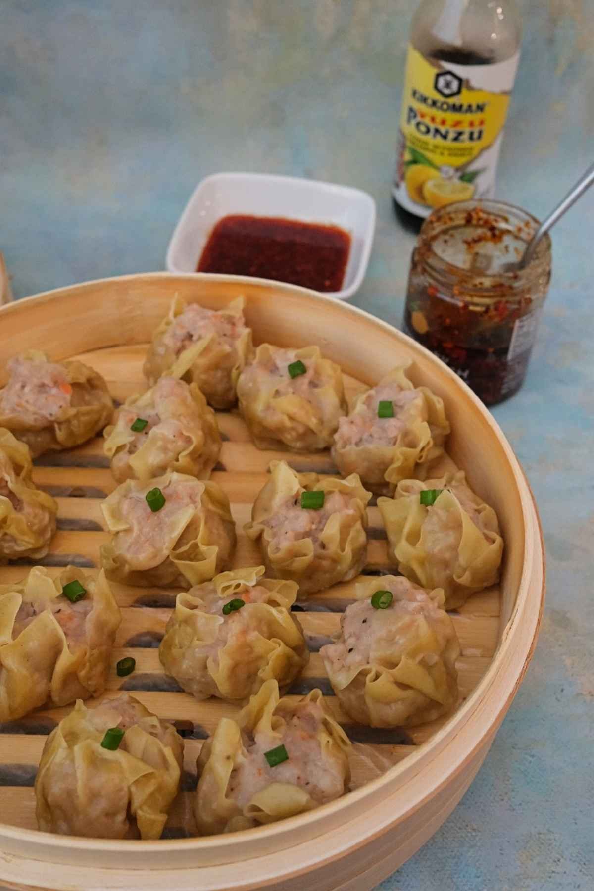 Steamed pork siomai in bamboo steamer with chili garlic dipping sauce.