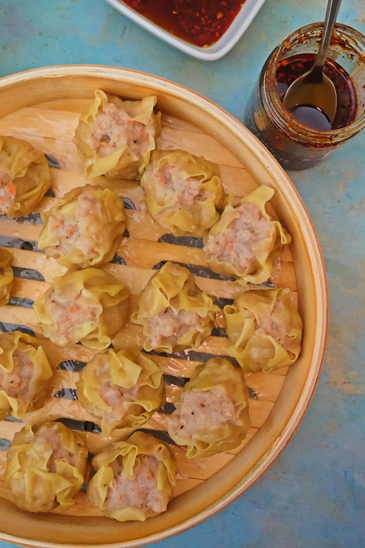 Steamed pork siomai in a bamboo steamer basket served with ponzu sauce and chili garlic on the side.