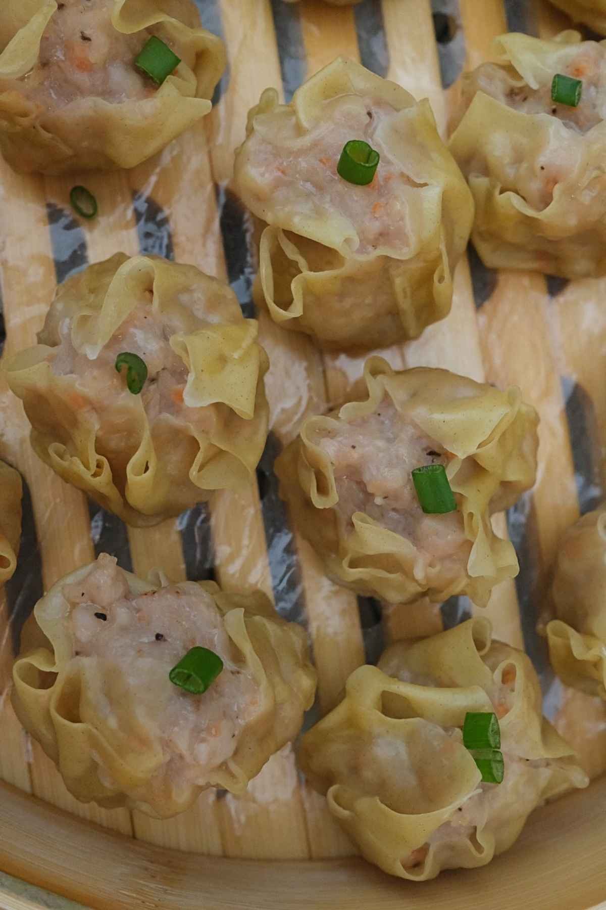 Close-up of steamed pork siomai garnished with chopped green onions in bamboo steamer.