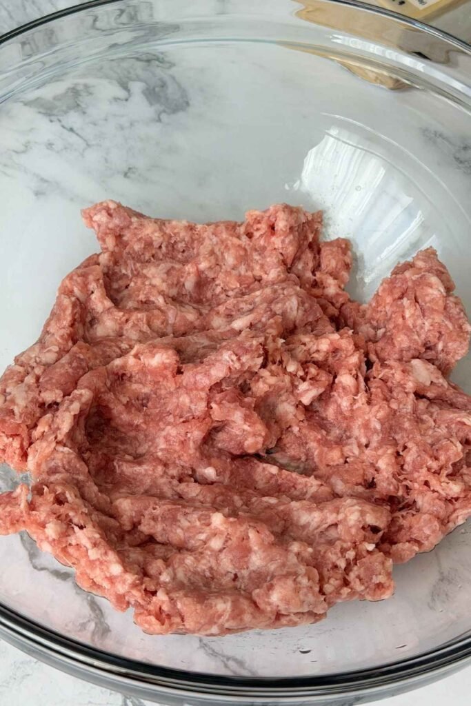 Ground pork placed in a glass mixing bowl.