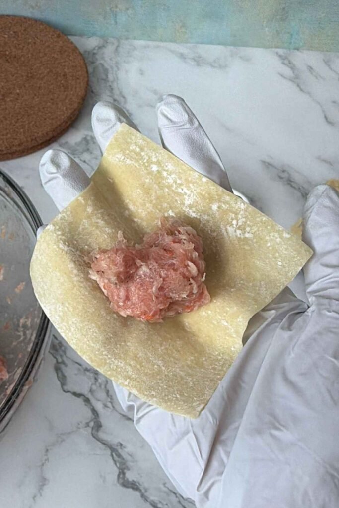 Scoop of pork and shrimp mixture centered on a wonton wrapper.