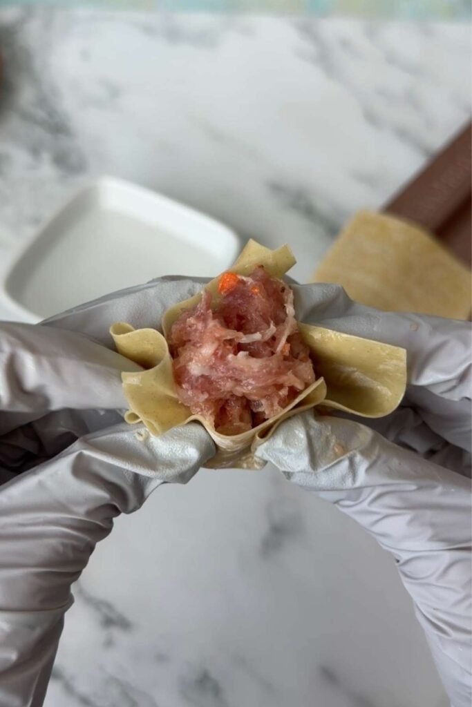 Folding and shaping pork siomai in a wonton wrapper by hand.