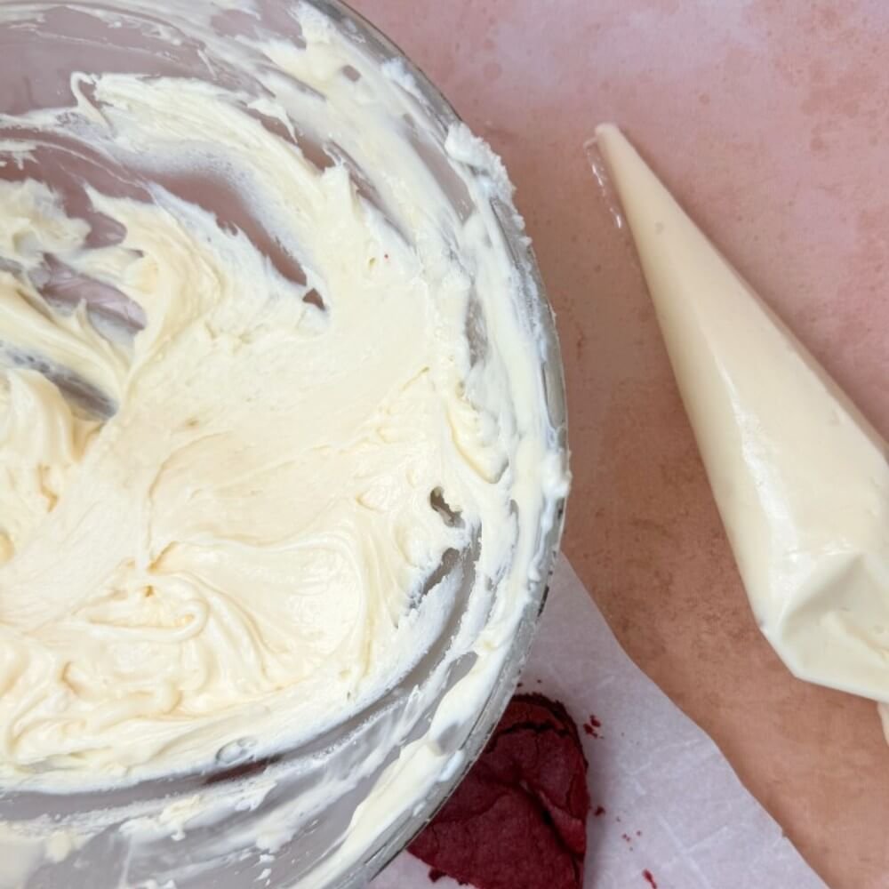 Cream cheese frosting in a bowl. Cream cheese frosting in a piping bag on the side.