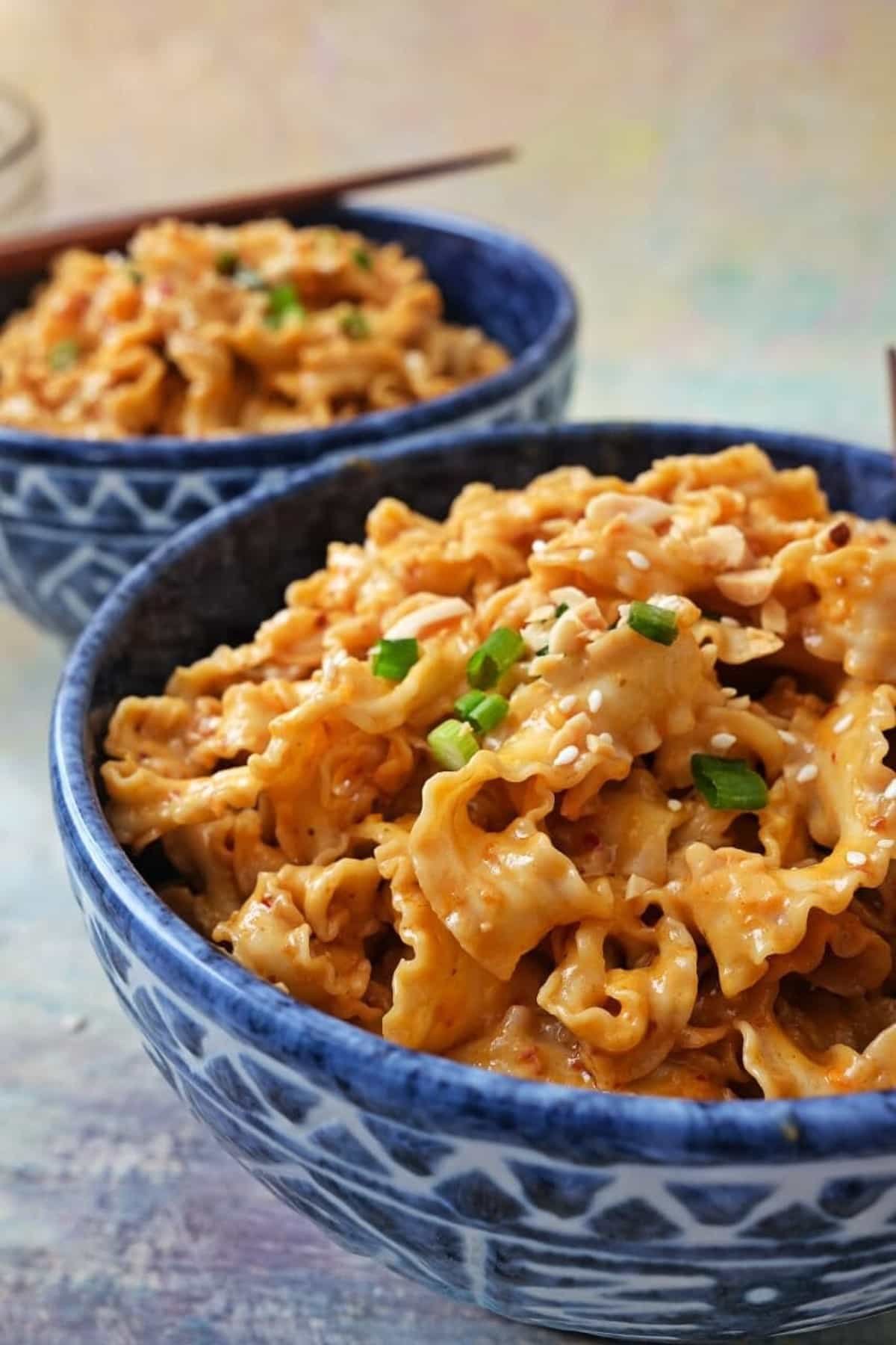 2 bowls of spicy peanut noodles, garnished with green onions and chopped nuts