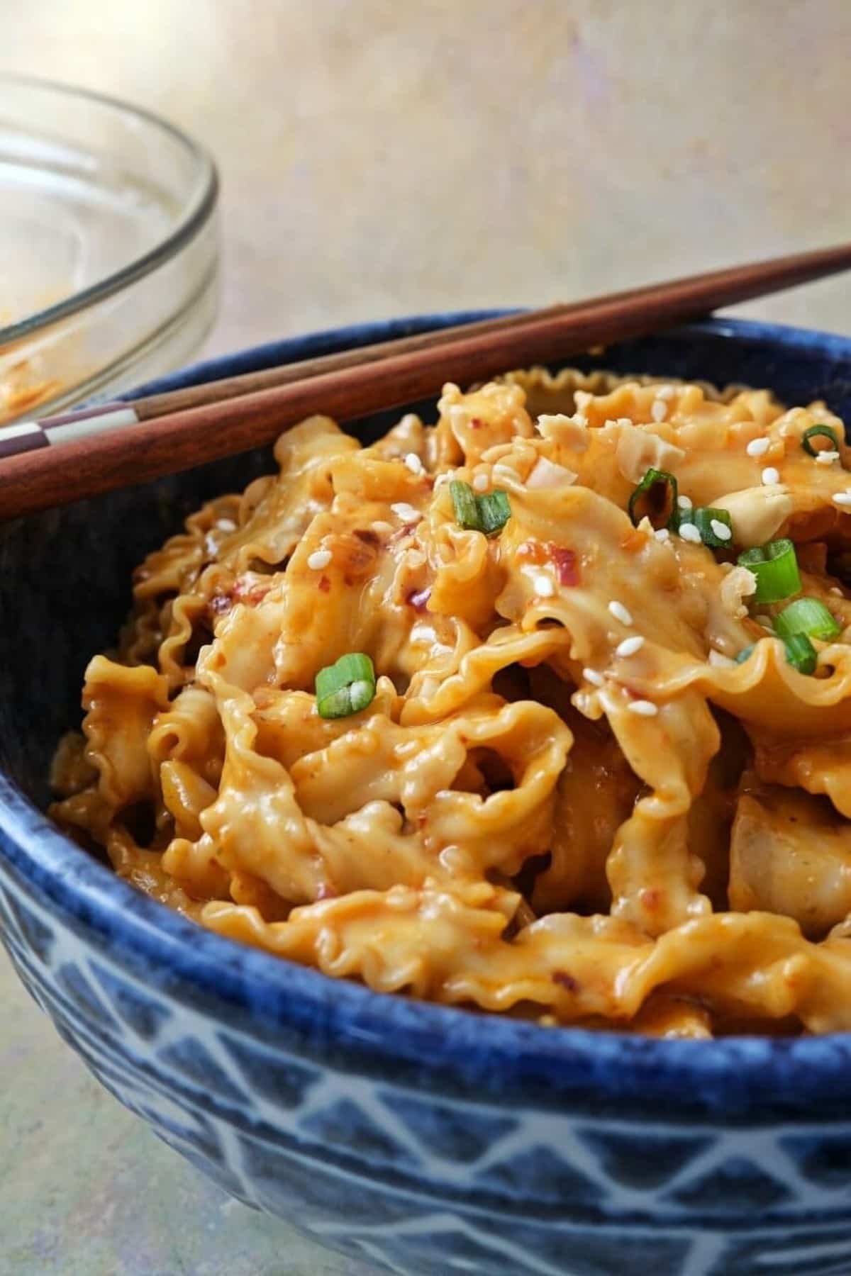 Spicy peanut butter noodles in a large bowl, with chopsticks on the side.