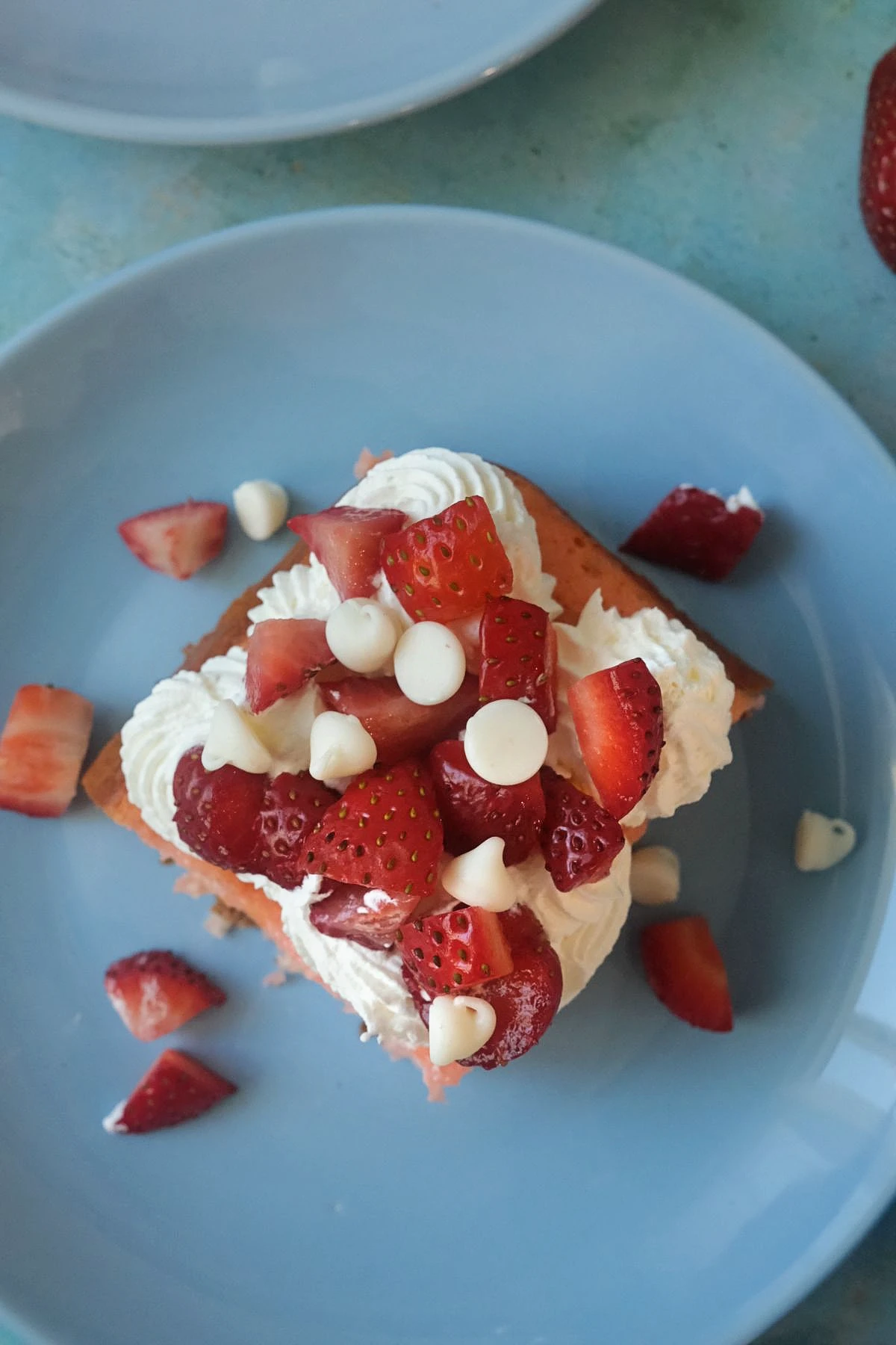 Single slice of strawberry earthquake cake topped with whipped cream and strawberries on a blue plate, with scattered white chocolate chips.
