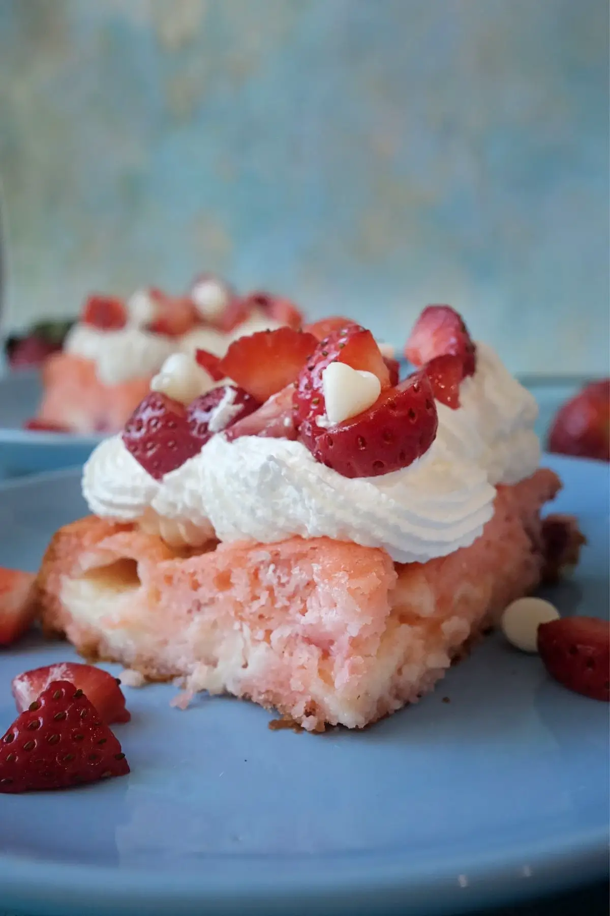 Close-up of a strawberry earthquake cake slice topped with whipped cream, strawberries, and white chocolate chips on a blue plate.